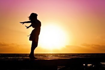 blog picture of woman stretching by the ocean with the sun coming up