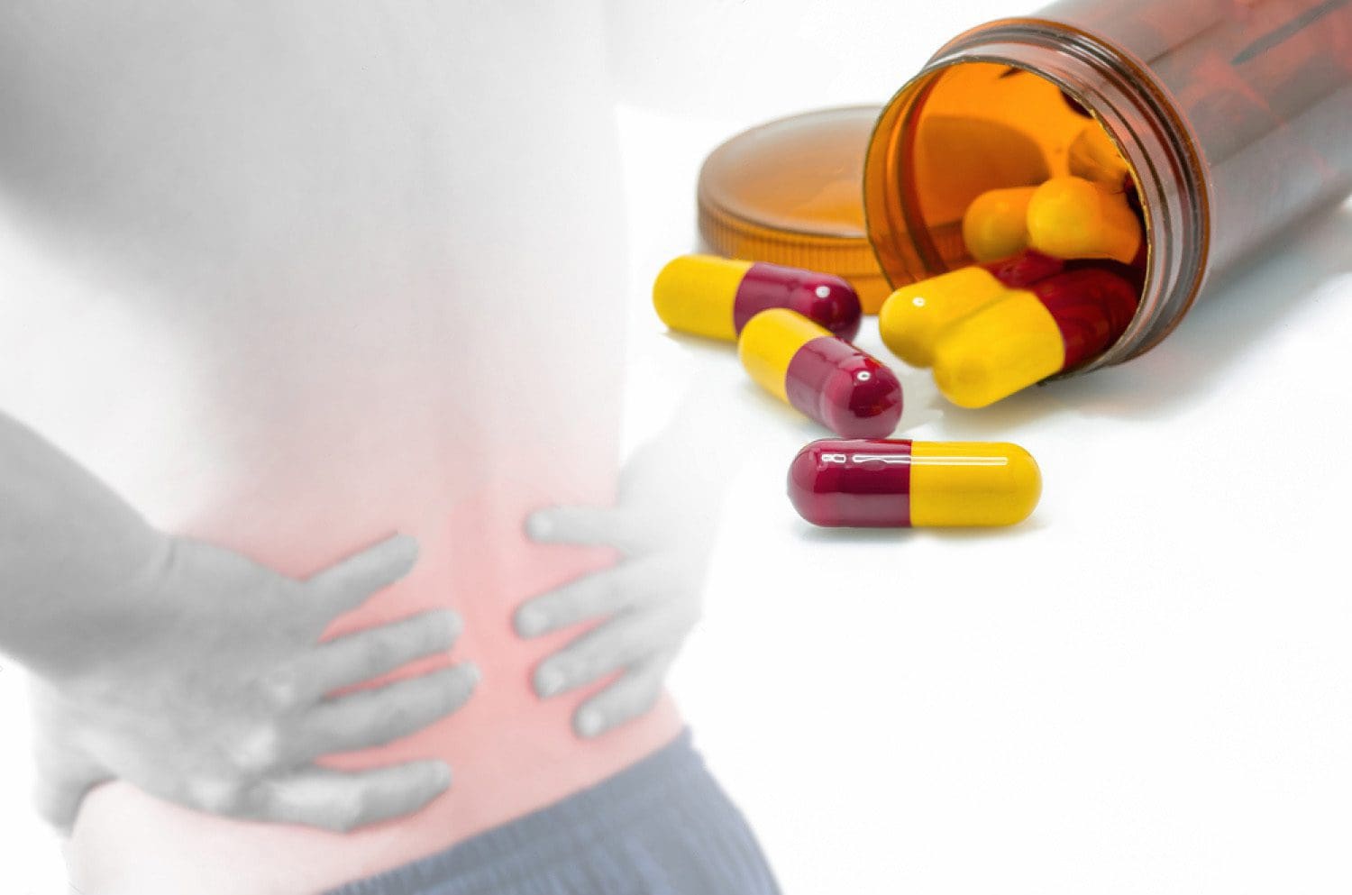 man grabbing lower back in pain and a bottle of pain medication open with capsules out of bottle