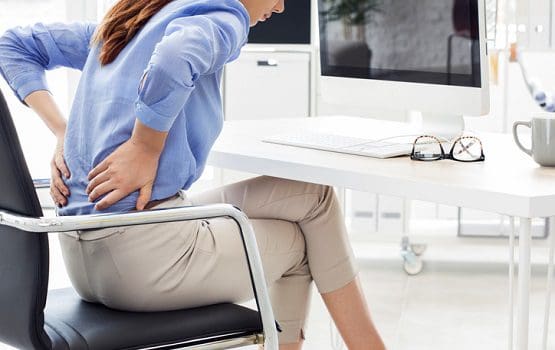 Woman holds her back as she experiences sciatica in the work setting.